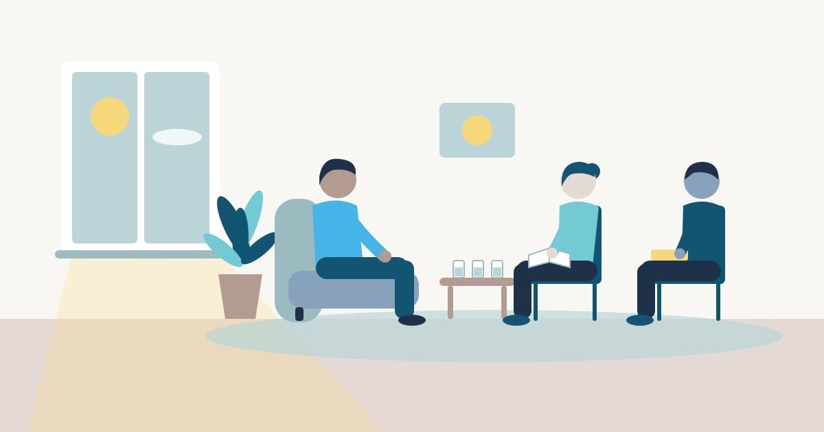 Persona adulta sentada en un sillón conversando con dos profesionales de la salud mental sentados frente a ella, una con una libreta y otra con una carpeta, en un consultorio luminoso con una planta y una ventana